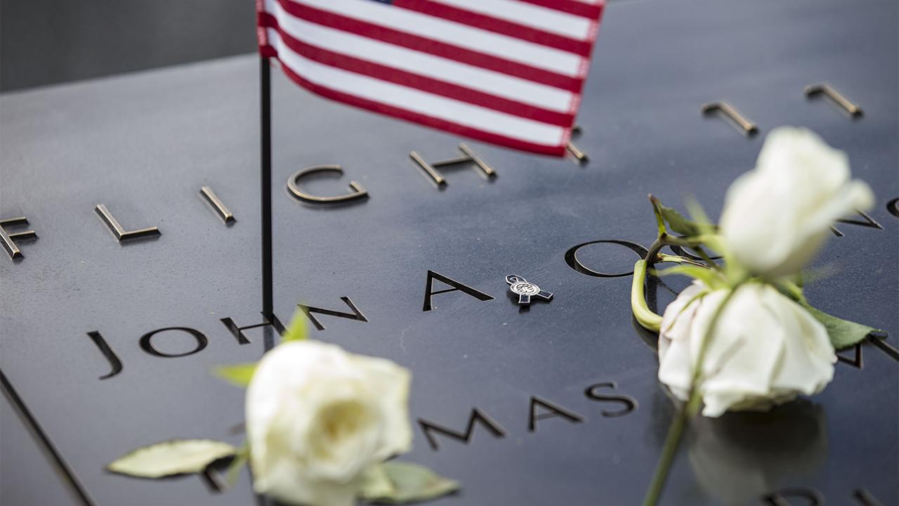 Several white roses and a small American flag have been placed at names on the Memorial. The names are under an inscription indicating they are American Airlines Flight 11 victims.