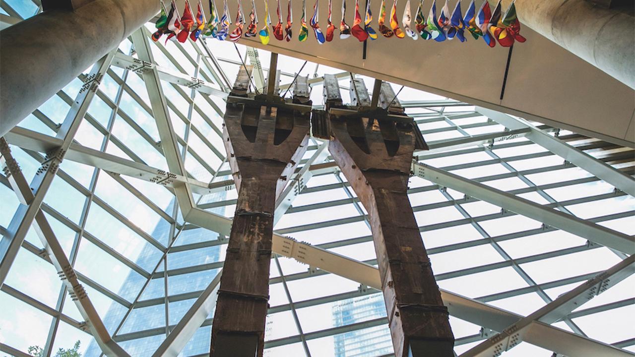 Two eighty-foot tall steel columns, known as the Tridents, tower over the interior of the museum Pavilion. One World Trade Center points skyward outside the windows.