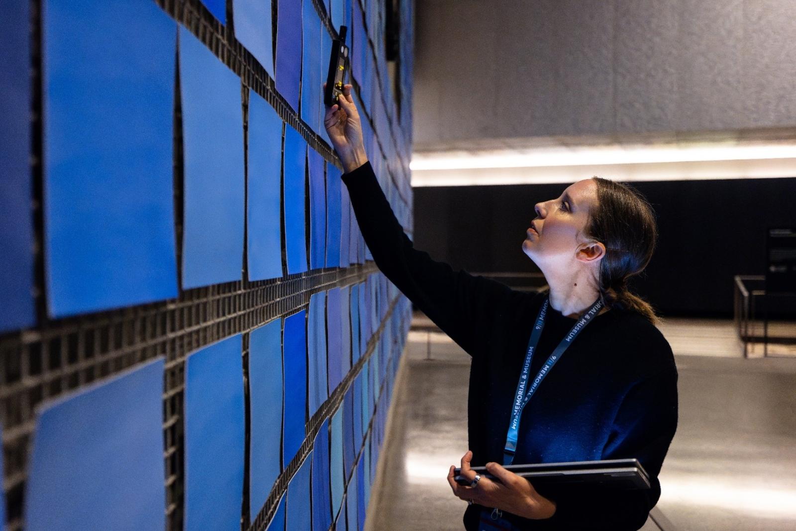 a woman holds a device up to the blue panels of an exhibit in the Museum