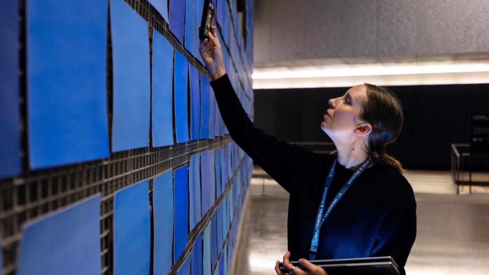 a woman holds a device up to the blue panels of an exhibit in the Museum