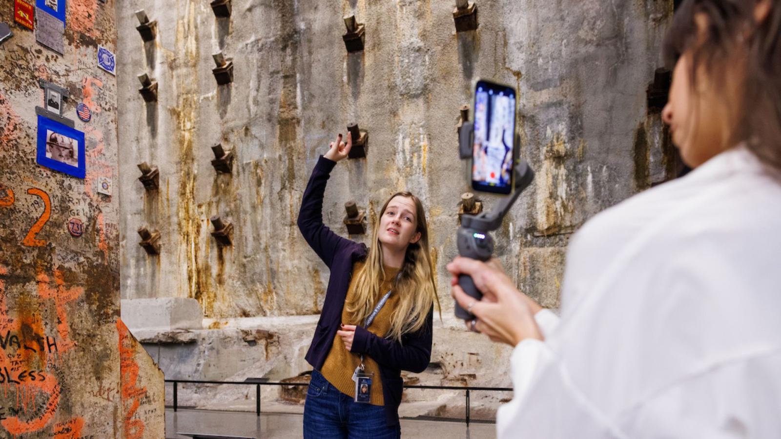 A woman stands in front of the Slurry Wall while another woman films her