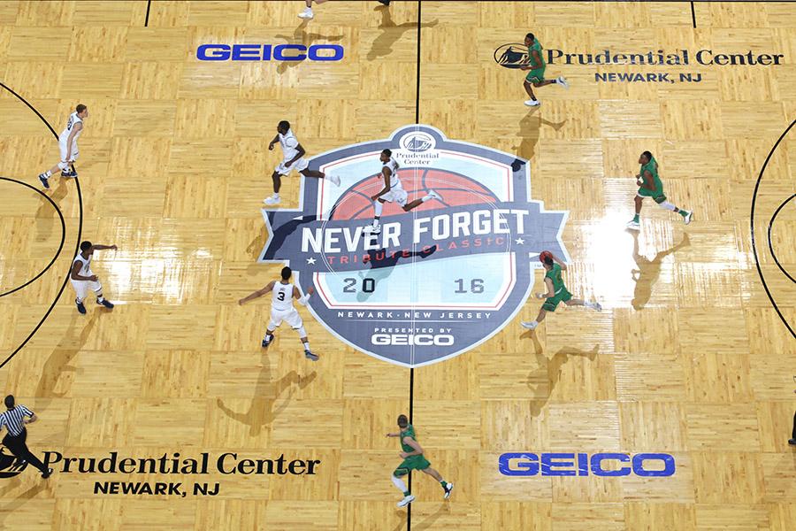 This view over a basketball court shows players taking part in the first-ever Never Forget Tribute Classic at Prudential Center in Newark. The name of the event is featured on a large decal at the center of the court.