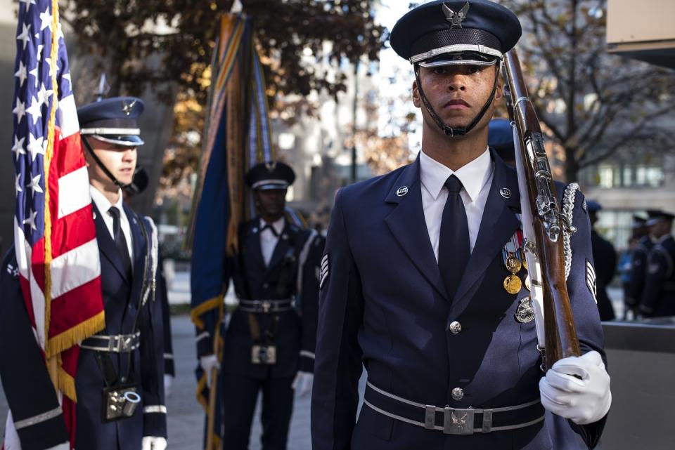 Three members of the U.S. Air Force are dressed formally and holding flags and rifles as they stand at Memorial plaza.