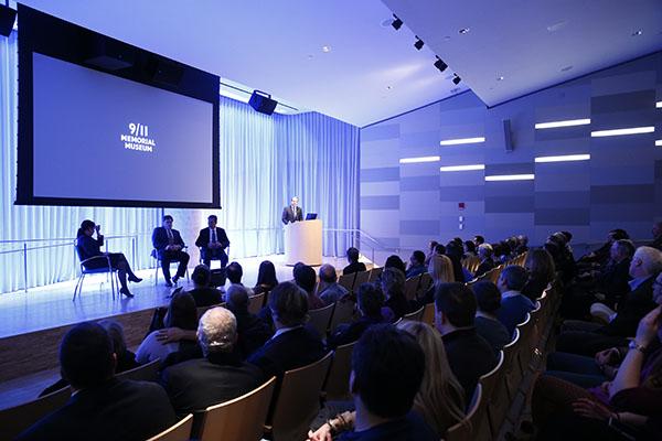 Dozens of audience members watch three men and a woman are seen onstage at the Museum’s Auditorium during a public program. 