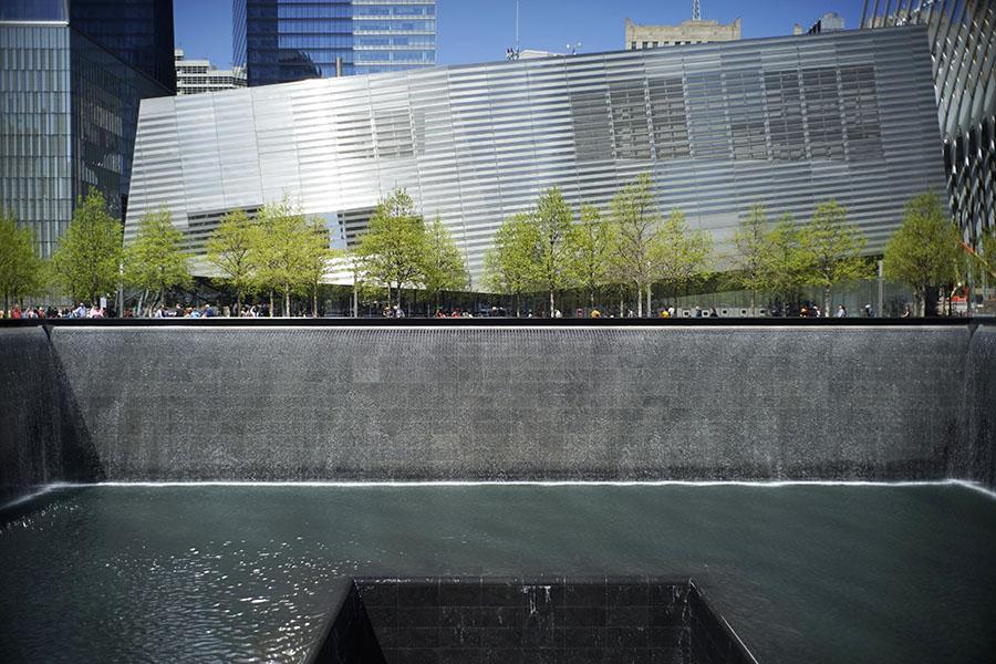 The Museum pavilion stands beside the south pool on a sunny day. The water from the pool is disappearing into a square hole in the center of the pool.