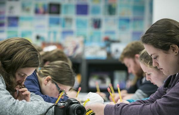 Students sit at tables and write with pencils as they work on an assignment at the Education Center in the Museum.