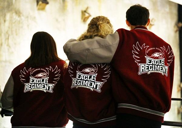 Three students wearing Marjory Stoneman Douglas High School letterman jackets stand beside each other as they visit the 9/11 Memorial Museum. One student has his left arm around another student.