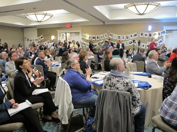 Audience members clap as they sit at circular tables while attending VOICES of September 11th. 