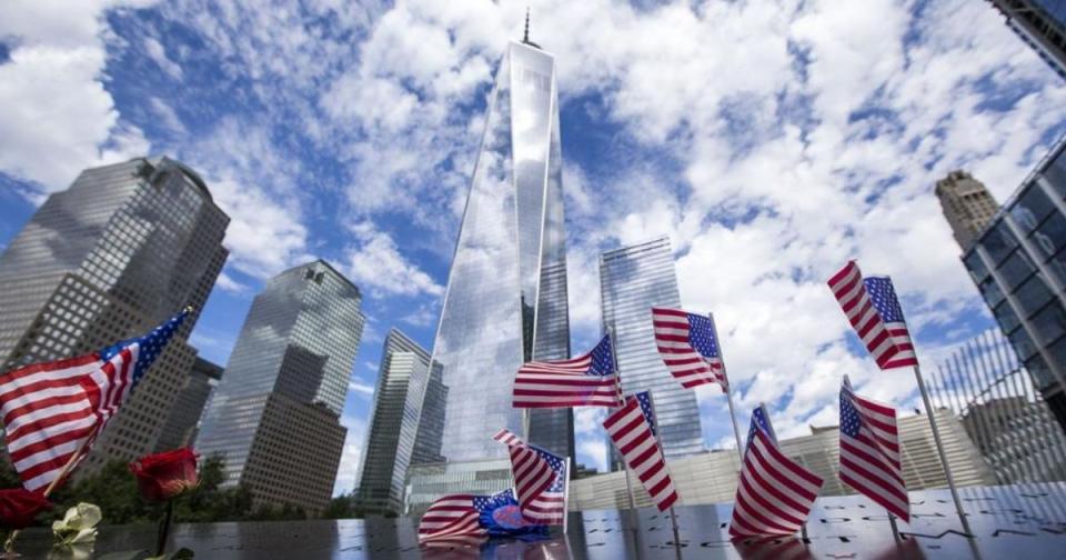 American flags are placed in the bronze parapets as One World Trade soars skyward amid white clouds and blue skies.