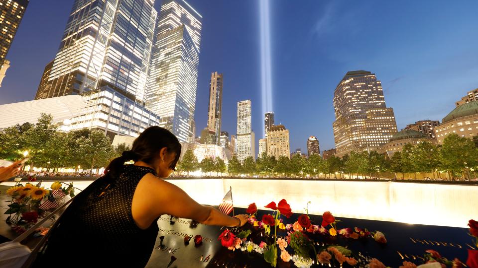 Back view of a woman placing flowers on the Memorial at night, with the Tribute in Light visible in the darkened sky